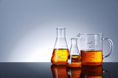 Photo of Different glassware with orange liquid on mirror surface against grey background, space for text
