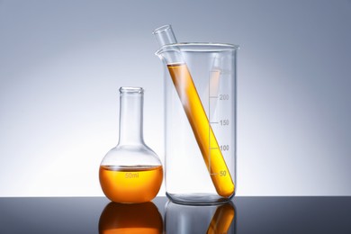 Photo of Different glassware with orange liquid on mirror surface against grey background