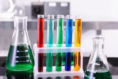 Photo of Test tubes and other glassware with different colorful liquids on table in laboratory, closeup