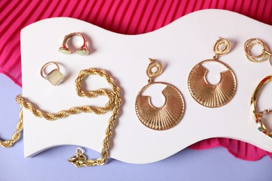 Photo of Stylish presentation of beautiful gold jewelry on violet background, top view