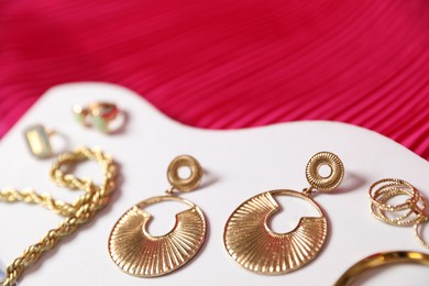 Photo of Stylish presentation of beautiful gold jewelry on pink fabric, closeup
