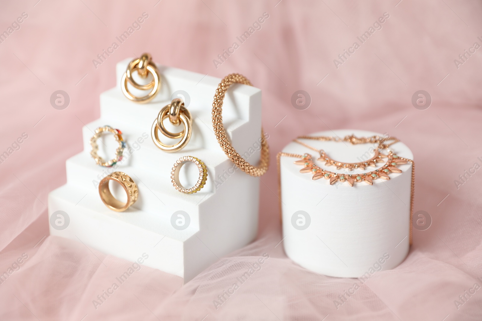Photo of Stylish presentation of beautiful gold jewelry on pink tulle fabric, closeup
