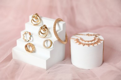 Photo of Stylish presentation of beautiful gold jewelry on pink tulle fabric, closeup