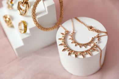 Photo of Stylish presentation of beautiful gold jewelry on pink tulle fabric, closeup