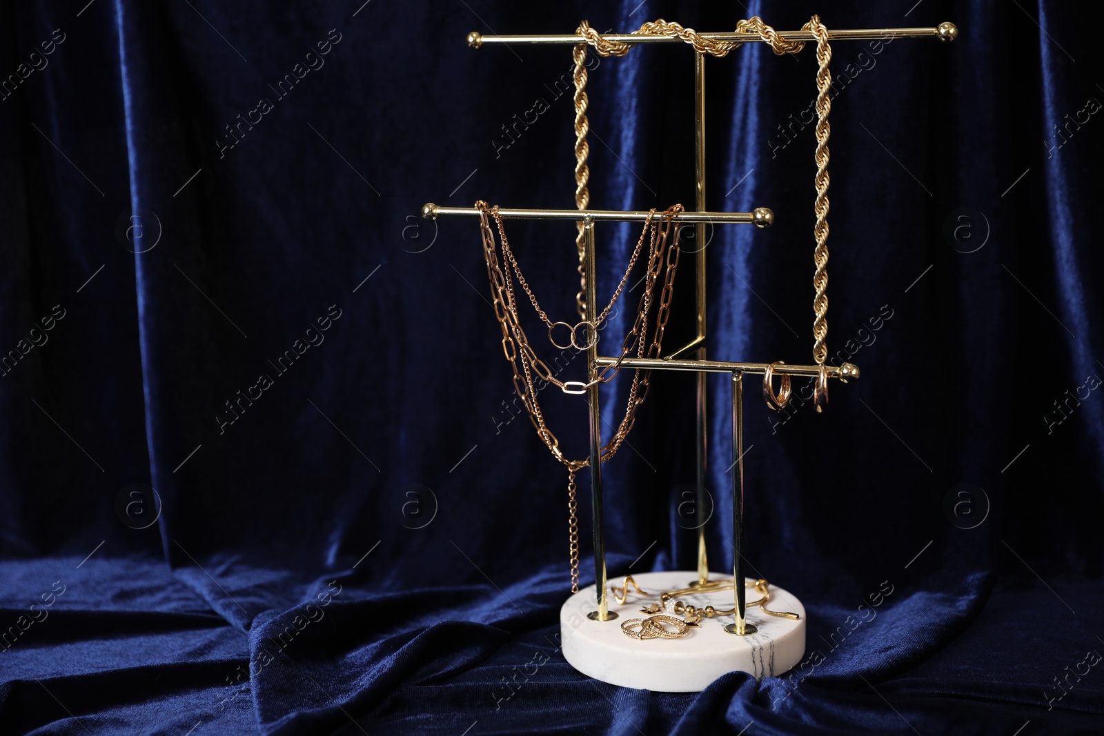 Photo of Stylish presentation of beautiful gold jewelry against dark blue fabric, space for text