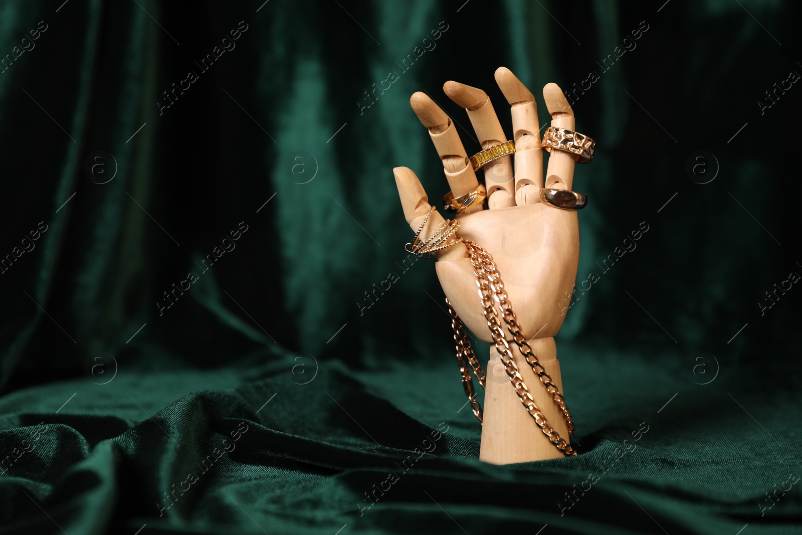 Photo of Mannequin hand with beautiful gold jewelry against dark green cloth, space for text