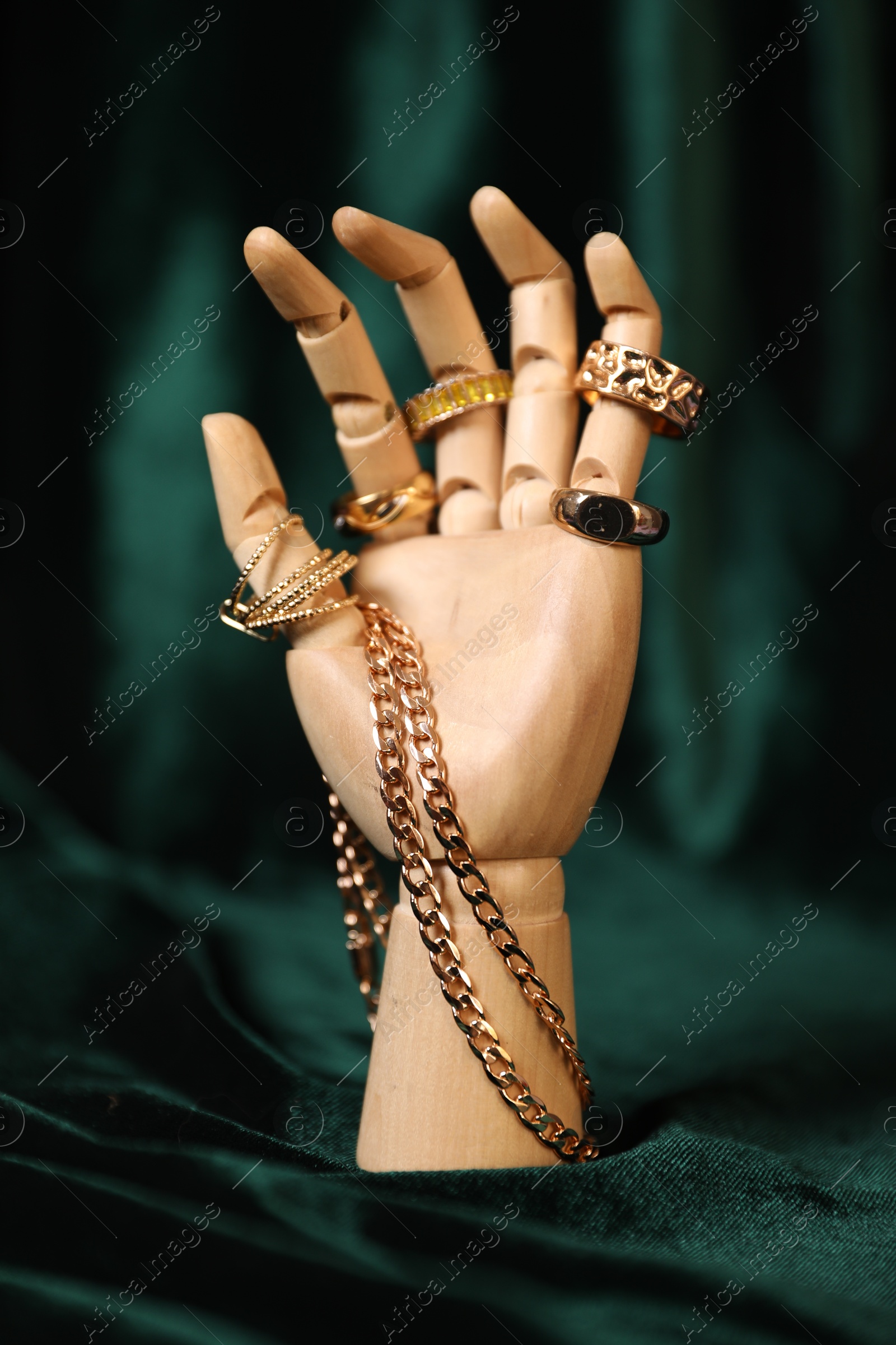 Photo of Mannequin hand with beautiful gold jewelry against dark green cloth
