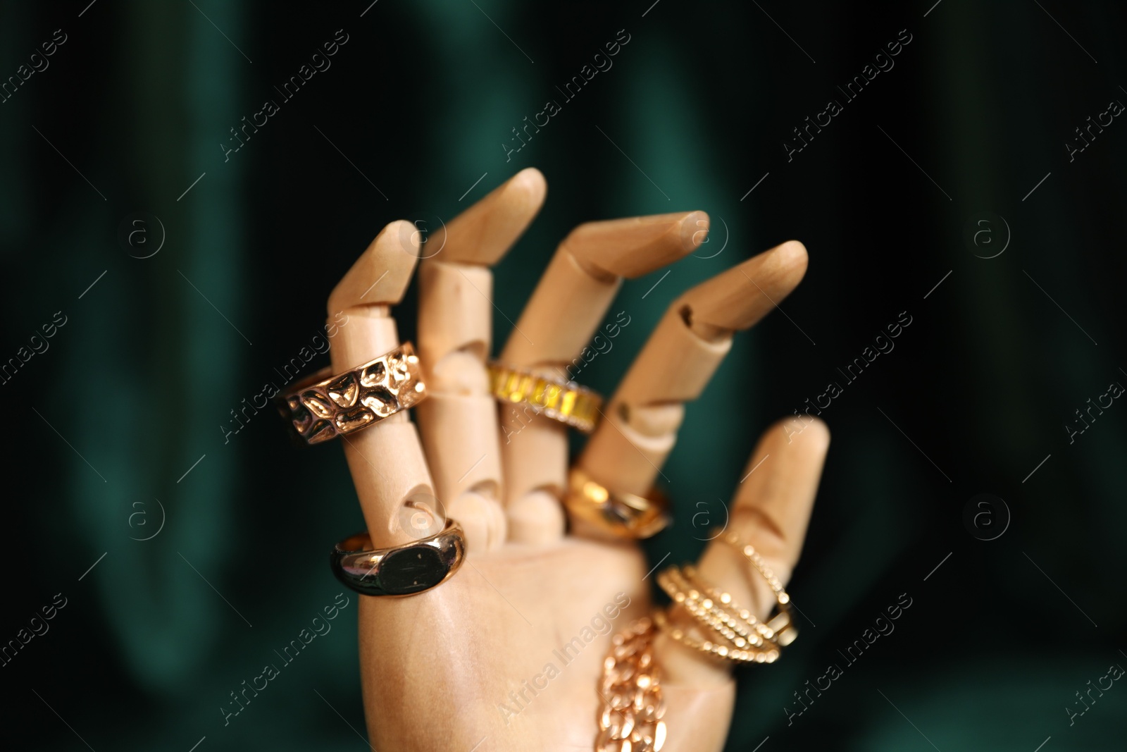 Photo of Mannequin hand with beautiful gold jewelry against dark green cloth, closeup