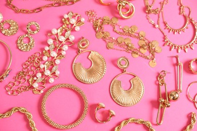 Photo of Beautiful gold jewelry on pink background, flat lay