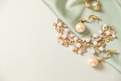 Photo of Beautiful gold jewelry and silk cloth on beige background, closeup. Space for text