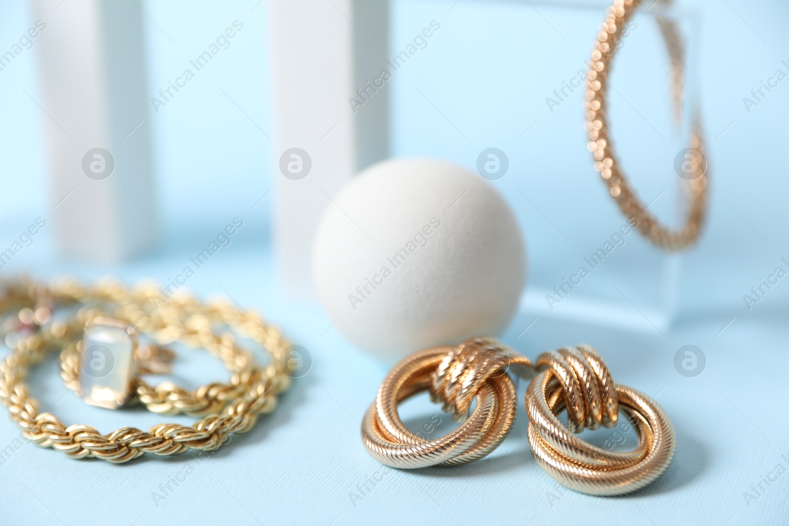 Photo of Stylish presentation of beautiful gold jewelry on light blue background, closeup