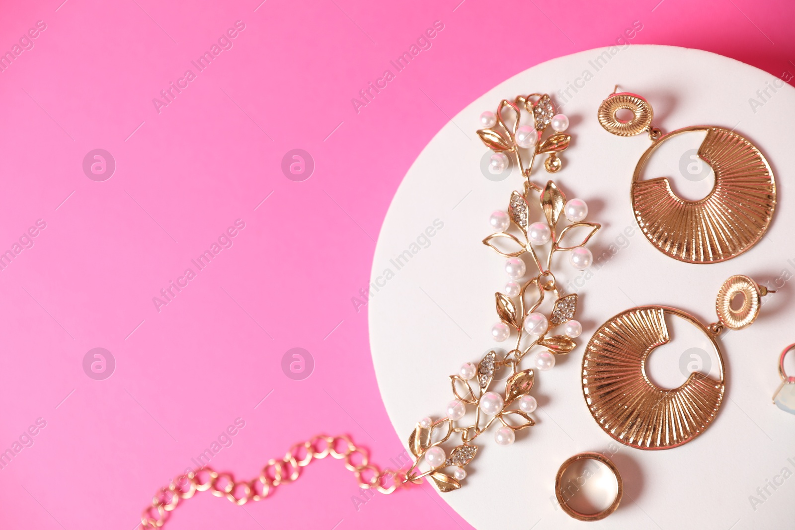 Photo of Stylish presentation of beautiful gold jewelry on pink background, top view. Space for text