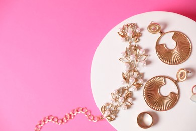 Photo of Stylish presentation of beautiful gold jewelry on pink background, top view. Space for text