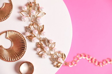 Photo of Stylish presentation of beautiful gold jewelry on pink background, top view. Space for text