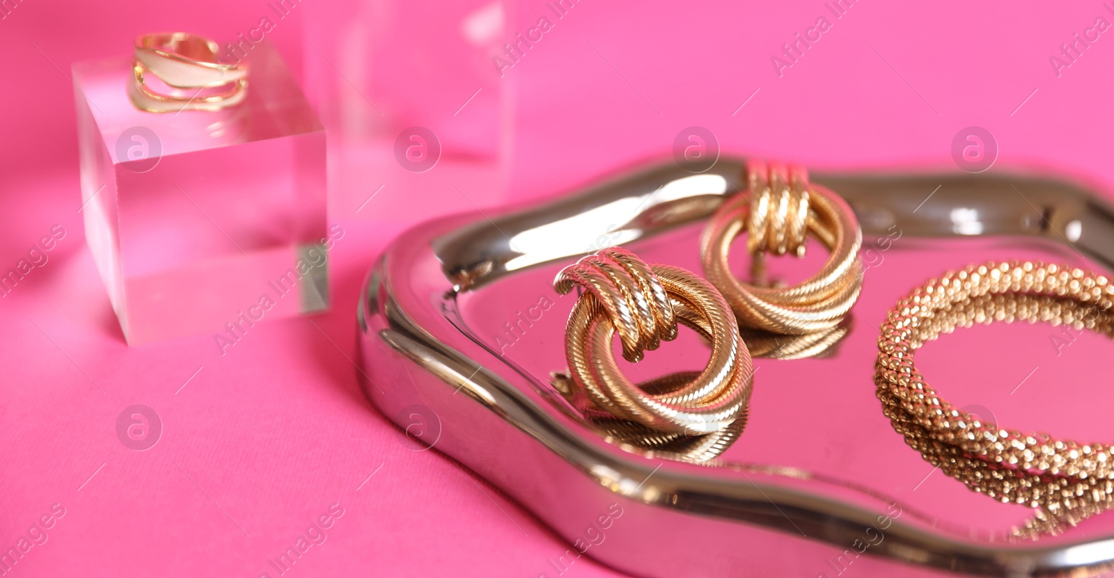 Photo of Stylish presentation of beautiful gold jewelry on pink background, closeup