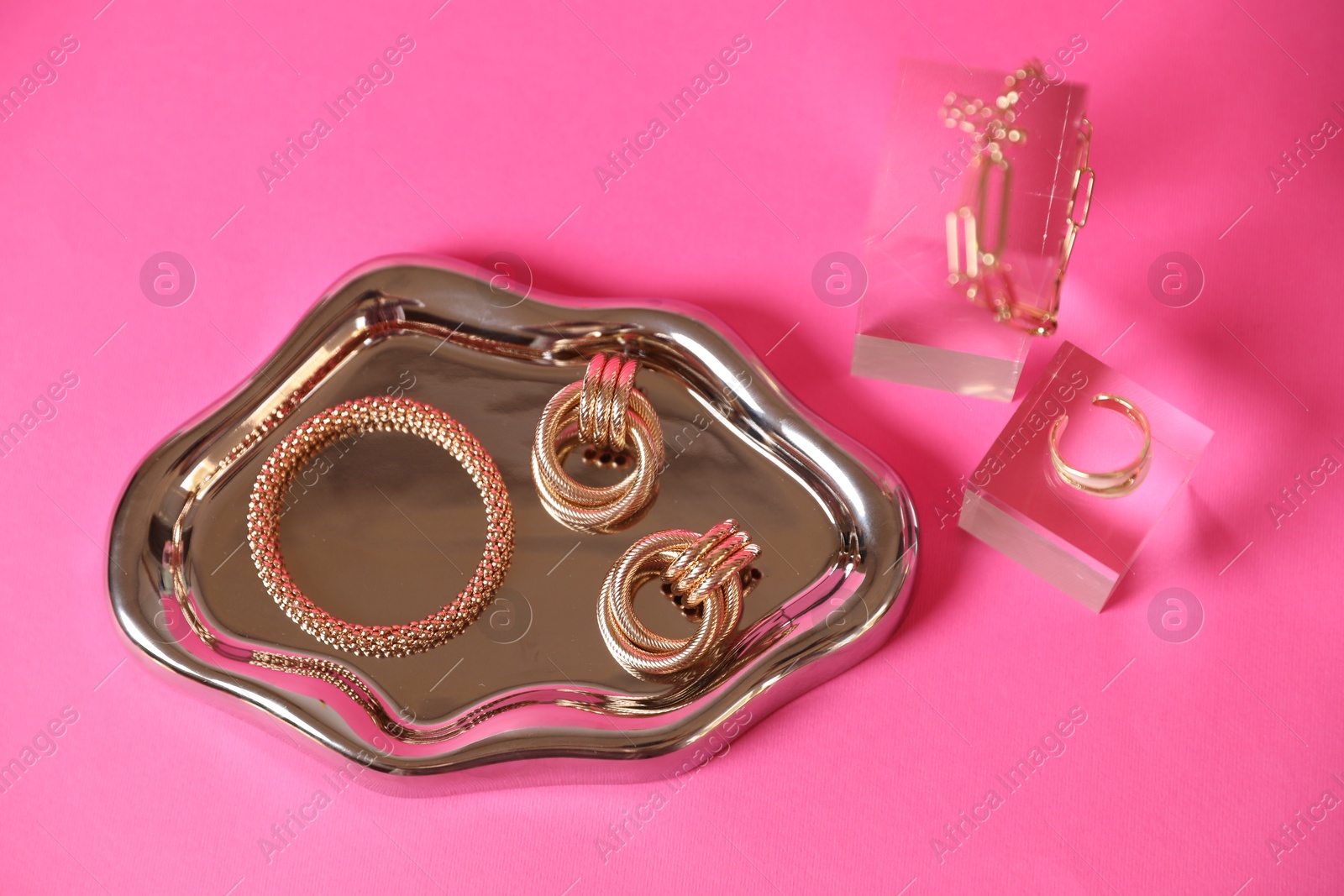 Photo of Stylish presentation of beautiful gold jewelry on pink background, above view