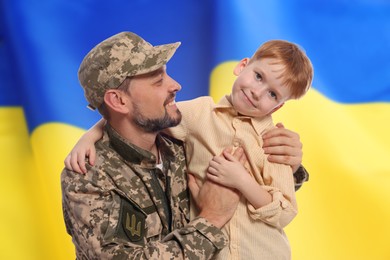 Image of Military man and his happy son against flag of Ukraine