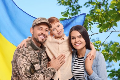 Image of Happy military man with his family and flag of Ukraine outdoors