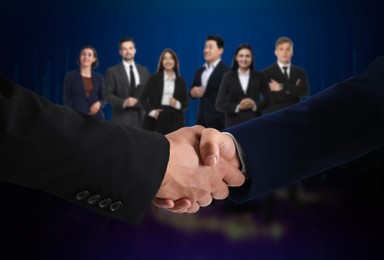 Image of Business partners shaking hands against group of people. Dark blue background