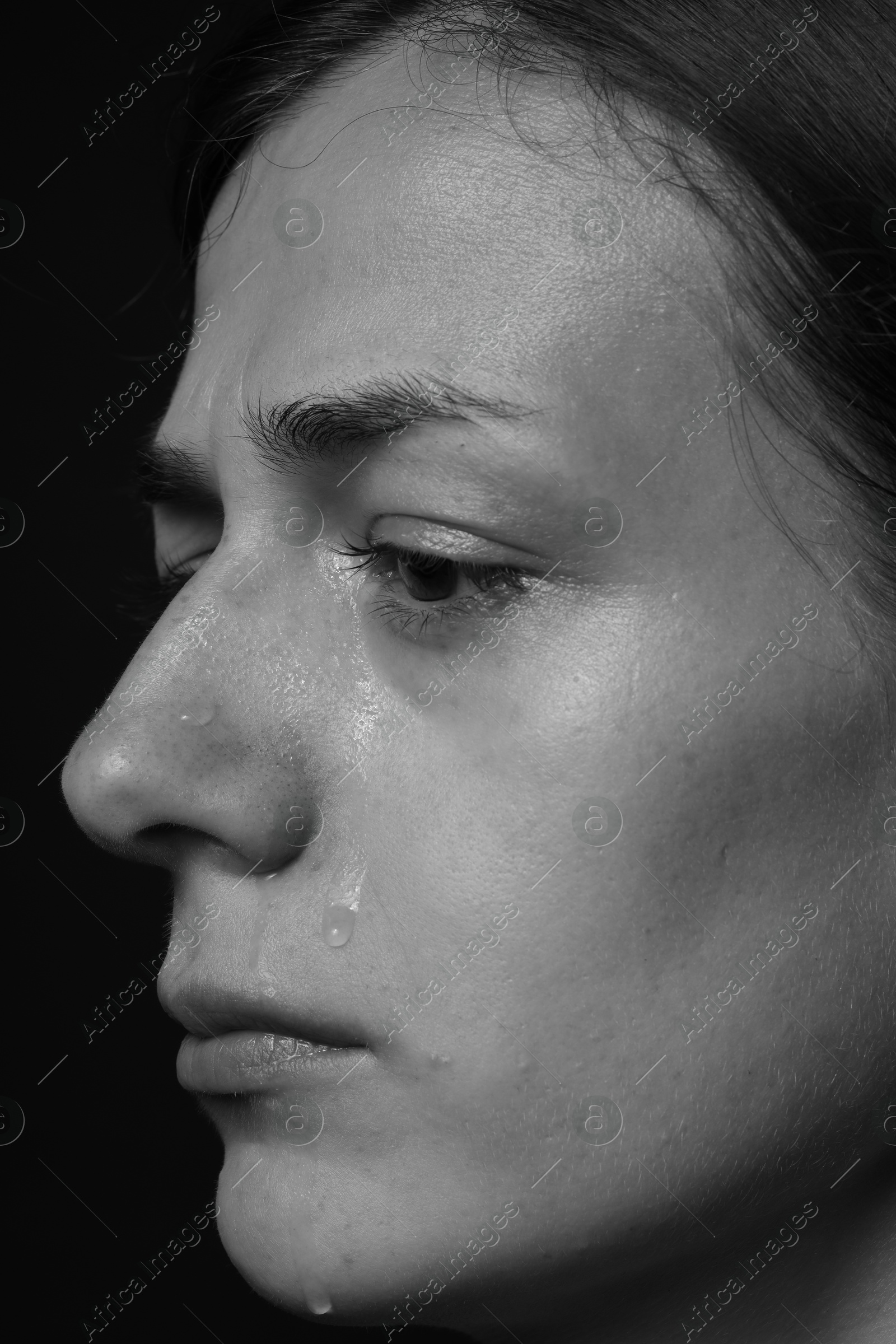 Photo of Sad woman crying on dark background, closeup. Black and white effect