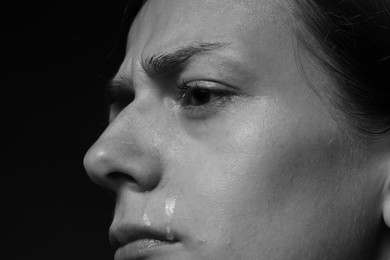 Photo of Sad woman crying on dark background, closeup. Black and white effect