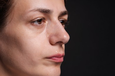 Photo of Sad woman crying on black background, closeup. Space for text