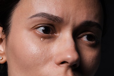 Photo of Sad woman crying on black background, closeup