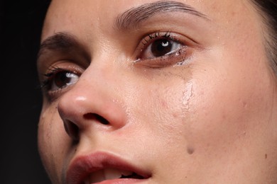 Photo of Sad woman crying on black background, closeup