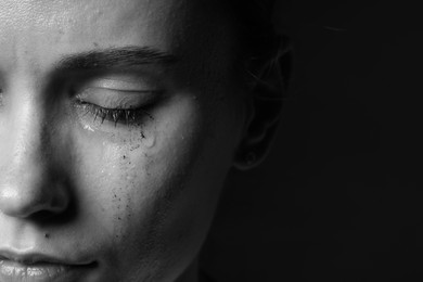 Photo of Sad woman crying on dark background, closeup. Black and white effect