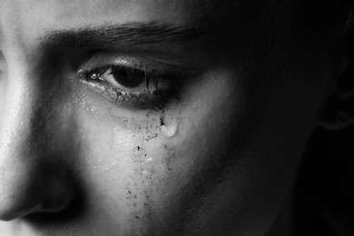 Photo of Sad woman crying on dark background, closeup. Black and white effect