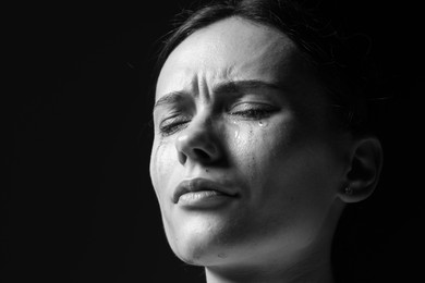Photo of Sad woman crying on dark background, closeup. Black and white effect