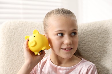 Photo of Pocket money. Little girl with piggy bank in armchair at home