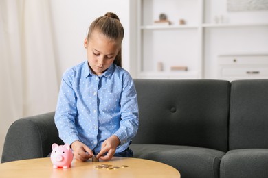 Photo of Little girl counting her pocket money at wooden table indoors, space for text