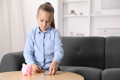 Photo of Little girl counting her pocket money at wooden table indoors, space for text
