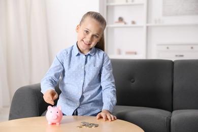 Photo of Little girl putting her pocket money into piggy bank at wooden table indoors, space for text