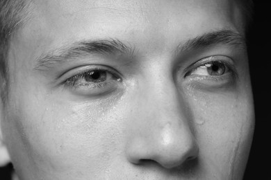 Photo of Sad man crying on dark background, closeup. Black and white effect