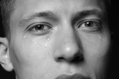 Photo of Sad man crying on dark background, closeup. Black and white effect