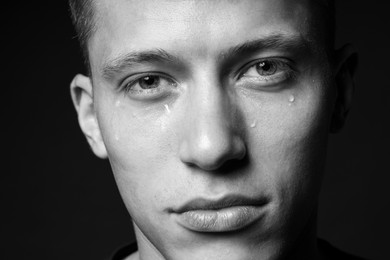 Photo of Sad man crying on dark background, closeup. Black and white effect
