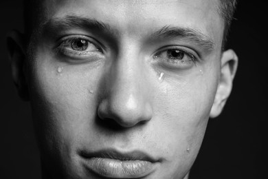 Photo of Sad man crying on dark background, closeup. Black and white effect