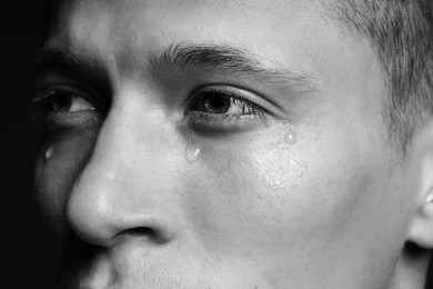 Photo of Sad man crying on dark background, closeup. Black and white effect