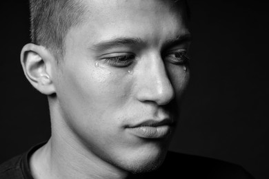Photo of Sad man crying on dark background, closeup. Black and white effect