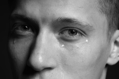 Photo of Sad man crying on dark background, closeup. Black and white effect