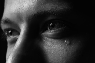 Photo of Sad man crying on dark background, closeup. Black and white effect