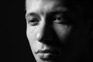 Photo of Sad man crying on dark background, closeup. Black and white effect