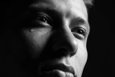 Photo of Sad man crying on dark background, closeup. Black and white effect