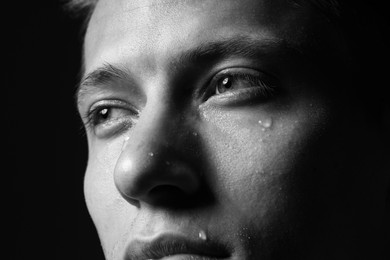 Photo of Sad man crying on dark background, closeup. Black and white effect