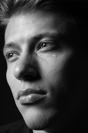 Photo of Sad man crying on dark background, closeup. Black and white effect