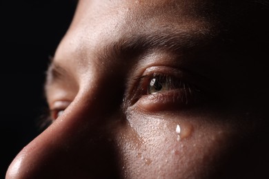 Photo of Sad man crying on black background, closeup