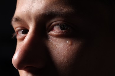 Photo of Sad man crying on black background, closeup