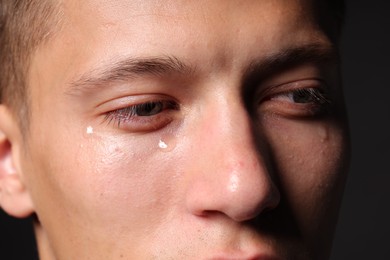 Photo of Sad man crying on black background, closeup
